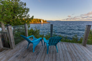 Two blue Muskoka chairs on a wood deck overlooking a Georgian Bay sunset and forested island
