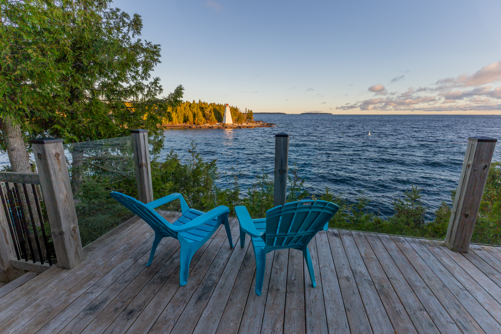 Two blue Muskoka chairs on a wood deck overlooking a Georgian Bay sunset and forested island