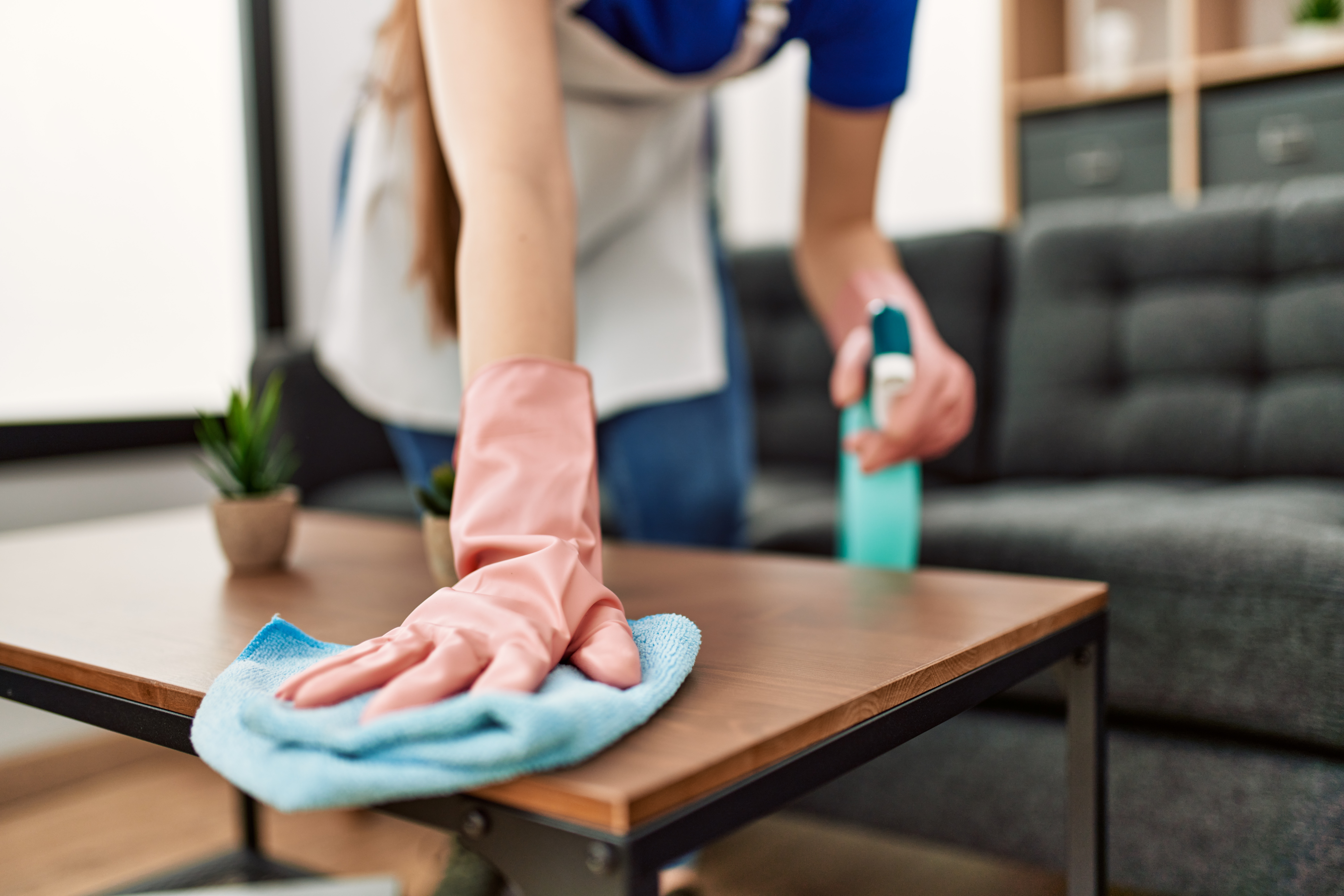 Person in pink rubber gloves wiping a coffee table with a cloth and spray cleaner